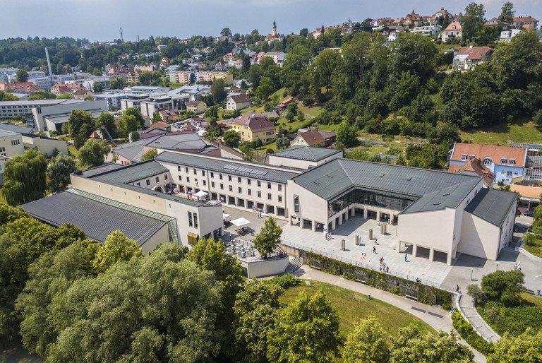 Zu sehen ist die Zentralbibliothek der Universit&auml;t Passau aus der Vogelperspektive. Menschen versammeln sich auf dem Vorplatz der Bibliothek und es herrscht ein sonniges warmes Wetter.