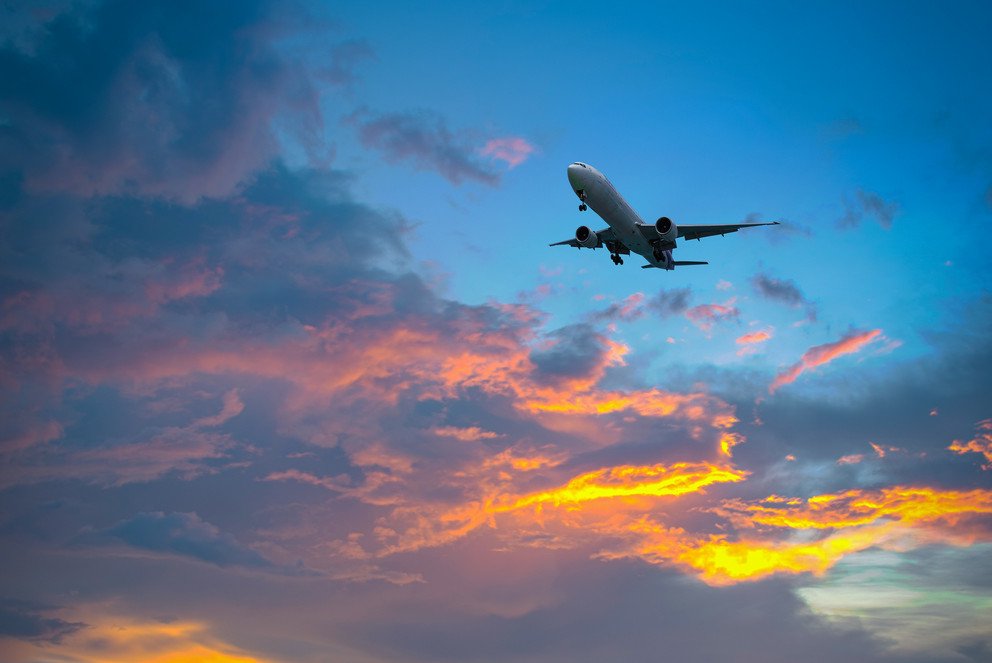 Ein Flugzeug in der D&auml;mmerung, von der Abendsonne gef&auml;rbte Wolken