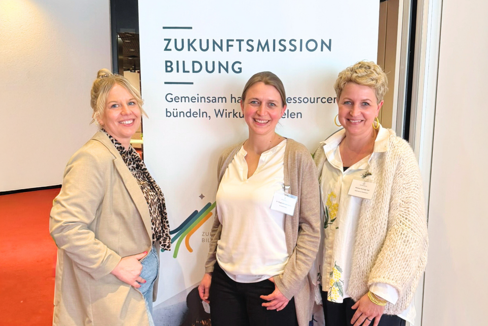 Das Passauer PReP Me-Team beim WandelBar-Kick-off in Bonn: Mittelschulmentorin Simone Rauch, Praktikumsamtsleiterin Dr. Magdalena Sonnleitner und Seminarrektorin Melanie Neulinger-Seil stehen nebeneinander vor einem Aufsteller des Stifterverbands, der mit dem Slogan "Zukunftsmission Bildung" wirbt