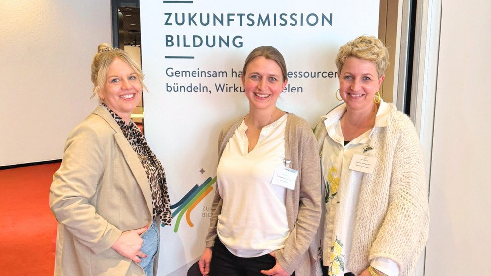 Drei Frauen stehen nebeneinander vor einem Aufsteller des Stifterverbands, der mit dem Slogan "Zukunftsmission Bildung" wirbt