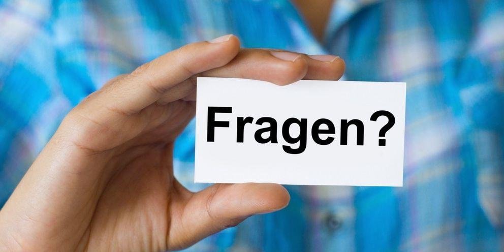 Es wird ein Schild mit dem Wort "Fragen" und einem Fragezeichen dahinter in die Kamera gehalten.