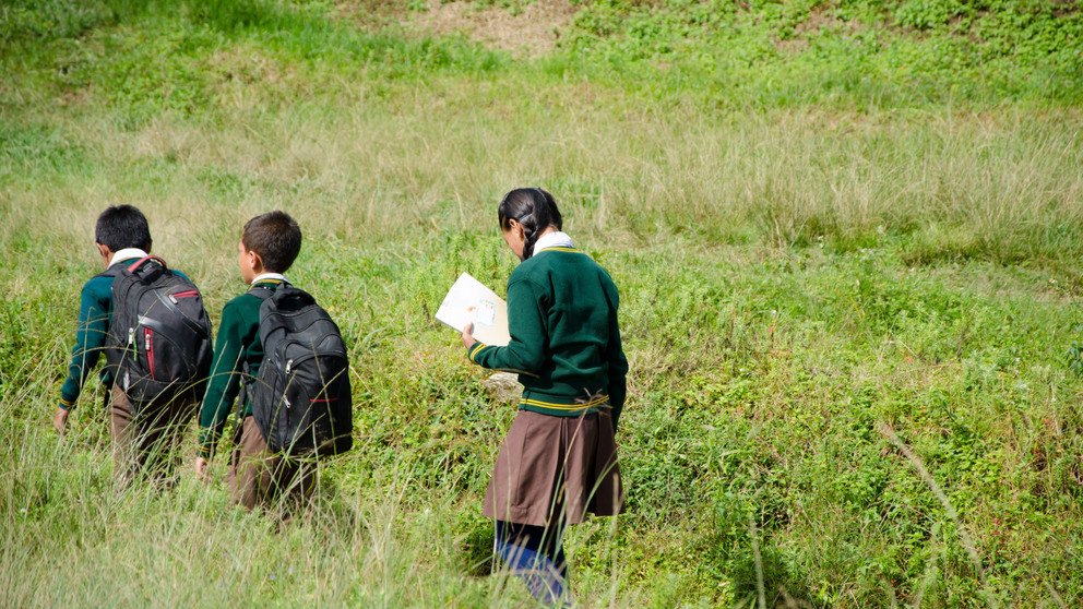 Zwei Jungen und ein M&auml;dchen in Schuluniform gehen durch eine Wiese