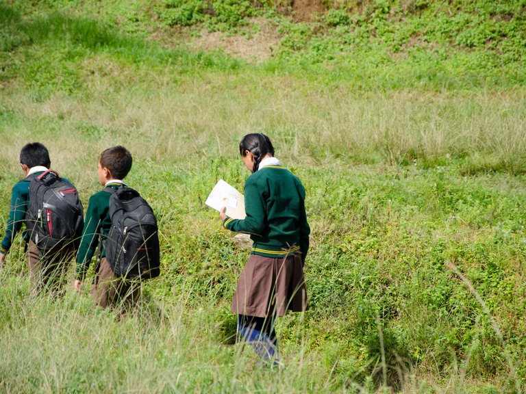 Zwei Jungen und ein M&auml;dchen in Schuluniform gehen durch eine Wiese