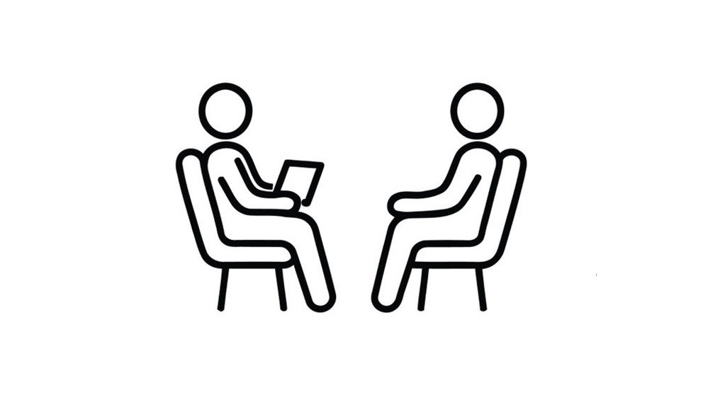 Piktogramm: Zwei Figuren sitzen sich auf St&uuml;hlen gegen&uuml;ber, die linke Figur h&auml;lt ein Blatt Papier