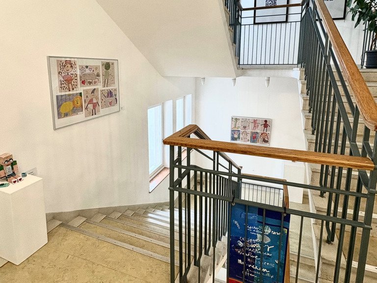 Ein Einblick in die Vernissage des ZLF. Zu sehen sind einige der Ausstellungsst&uuml;cke des Kunstwettbewerbs, verteilt im Treppenhaus des Institutsgeb&auml;udes der Uni Passau.