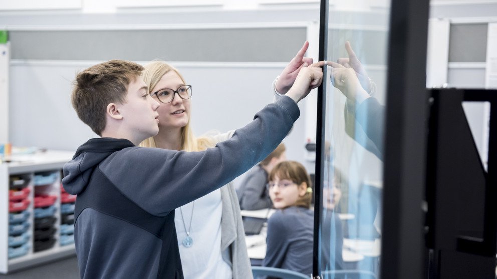 Eine Sch&uuml;ler und eine junge Studentin arbeiten gemeinsam interessiert an einem digitalen Smartboard.