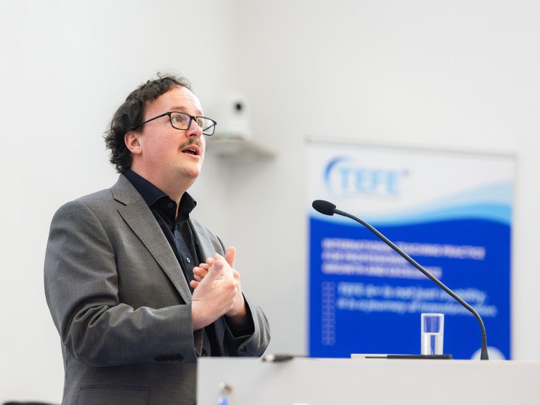 Dr. Jonas Scharfenberg von der Universit&auml;t Passau h&auml;lt am Rednerpult seinen Vortrag