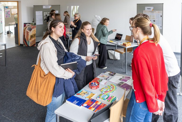 zwei junge Frauen stehen an einem Info-Stand und reden mit der Frau und dem Mann, die den Info-Stand betreuen