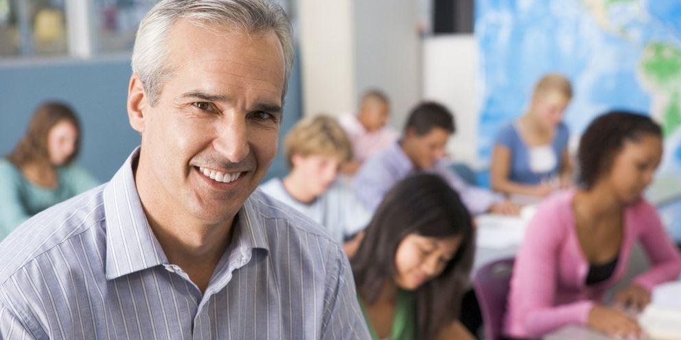Informationen für Lehrkräfte Ein Lehrer steht im Klassenzimmer vor seinen Schülern und guckt in die Kamera.
