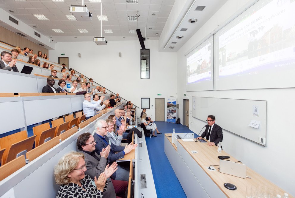 Ein H&ouml;rsaal an der S&uuml;db&ouml;hmischen Universit&auml;t Budweis, ungef&auml;hr zu zwei Dritteln gef&uuml;llt. Die Personen in den Stuhlreihen applaudieren dem vorne stehenden Redner.