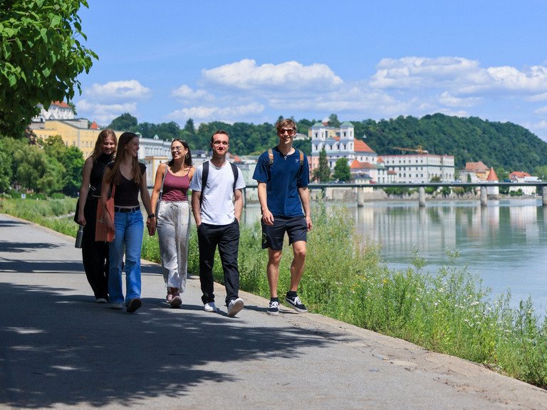 drei Studentinnen und zwei Studenten gehen gemeinsam am Inn entlang