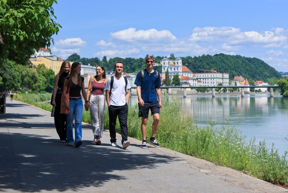 drei Studentinnen und zwei Studenten gehen gemeinsam am Inn entlang