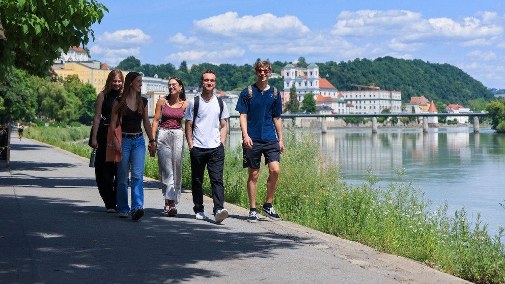 drei Studentinnen und zwei Studenten gehen gemeinsam am Inn entlang
